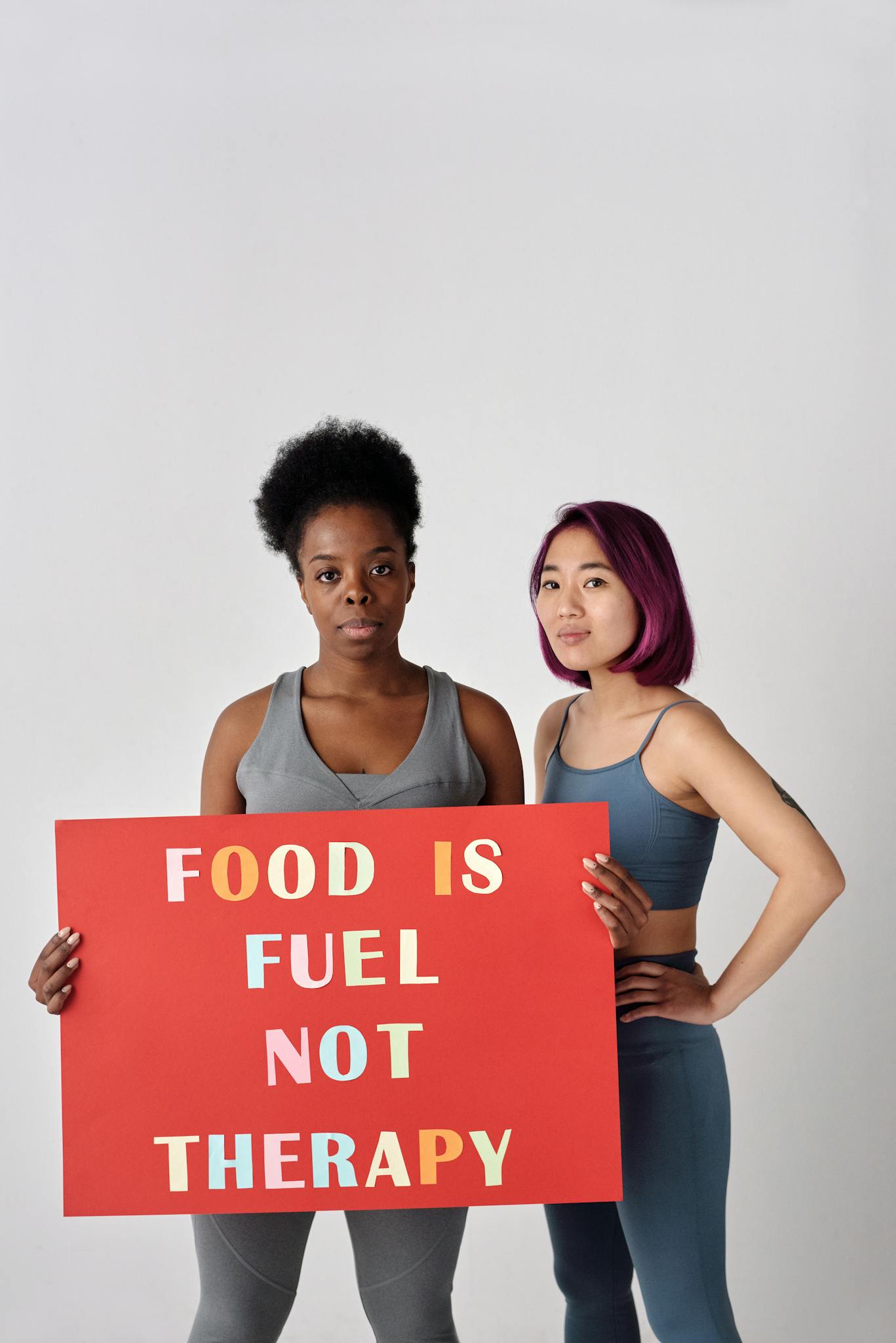 Two women stand confident with a sign promoting healthy food habits in a studio setting.